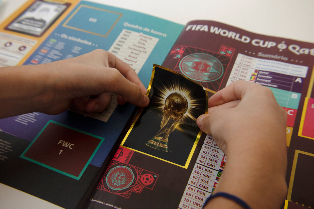A person placing a FIFA World Cup sticker into a collection album, showcasing the sticker collection experience.