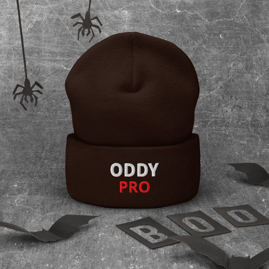 Oddy Pro Cuffed Beanie in brown with bold text, lying on a textured background with Halloween decorations.